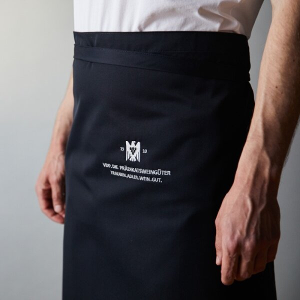 A figure wearing a black apron with the VDP logo embroidered on it. The mans arms are visible at his sides.