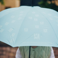 A woman is carrying a turquoise umbrella printed with white eagles.